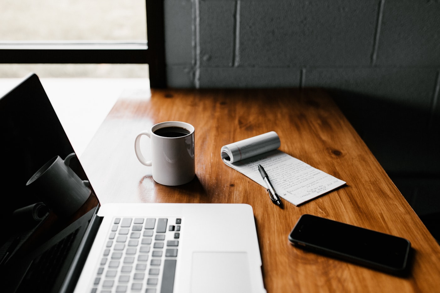 Laptop, coffee, and a notebook on a wooden desk